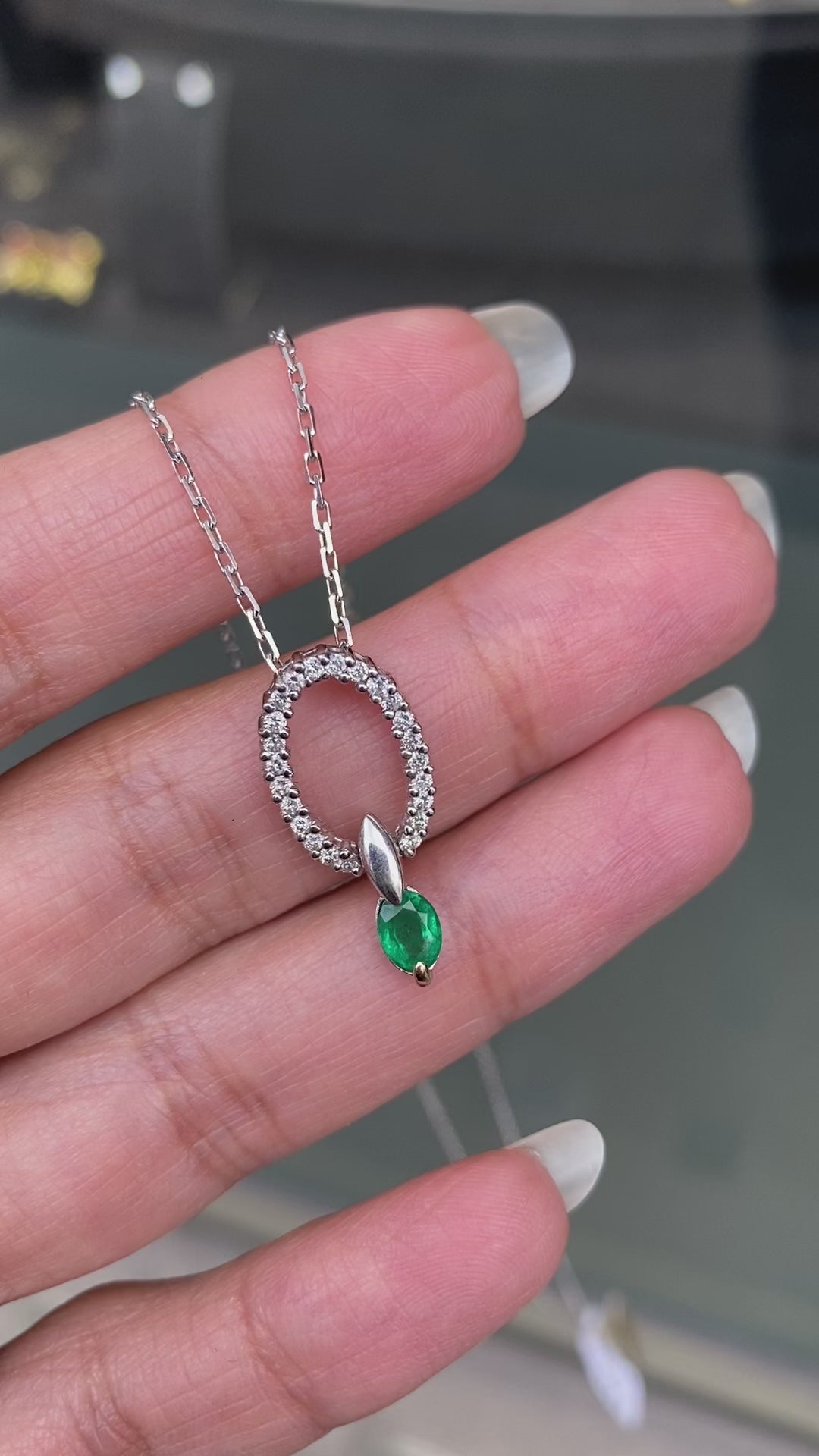 An 18 carat white gold oval pendant featuring a central emerald, surrounded by round brilliant cut diamonds set in a claw-like design.