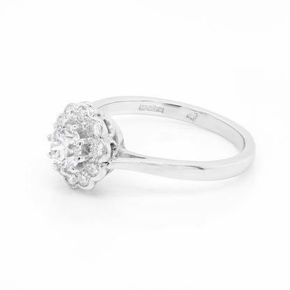 side view of a round brilliant cut diamond ring with smaller round brilliant cut diamonds set in a daisy cluster design, mounted in a platinum band.